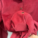 Prototype, détail du velours côtelé rouge et du poignet boutonné avec bouton foncé cerclé de doré